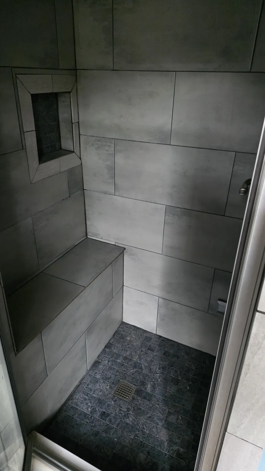 Gray tiled walk-in shower with bench and niche